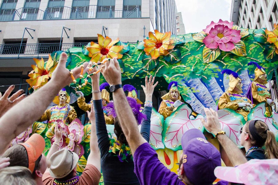 Crowd with arms up to catch "throws" from float with colorful, large artificial flowers at Mardi Gras parade