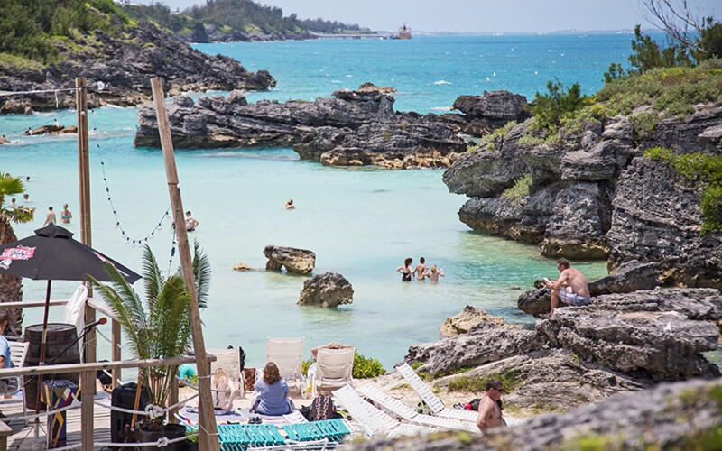 Short, rocky gray cliffs surround bay, with a few people in water or sitting on shore