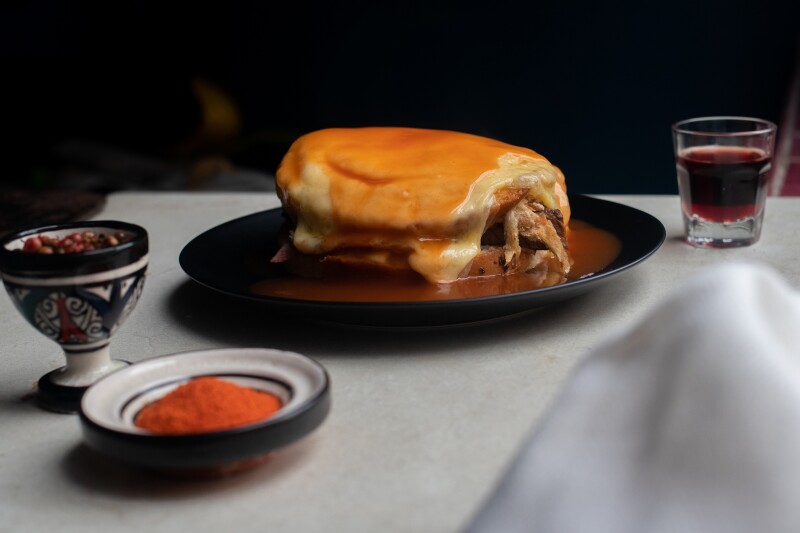 A traditional Francesinha sandwich in Porto topped with grilled cheese and surrounded by tomato sauce