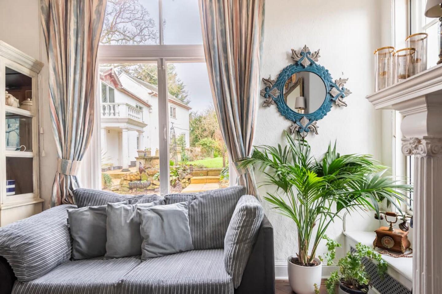 اتاق نشیمن با کاناپه خاکستری مدرن در مقابل یک پنجره با نمایی از یک خانه روستایی گرجستانی