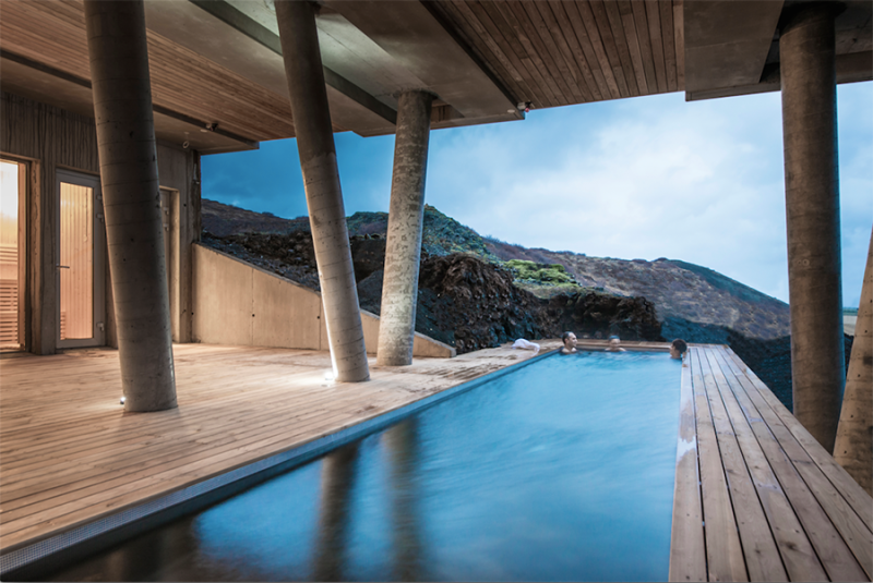 Long pool surrounded by wooden deck and roof at Ion Adventure Hotel; a few soakers at far end of pool