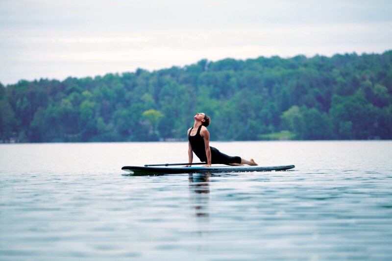 A person doing a yoga stretch on a stand-up paddleboard in a lake at Canyon Ranch Lenox