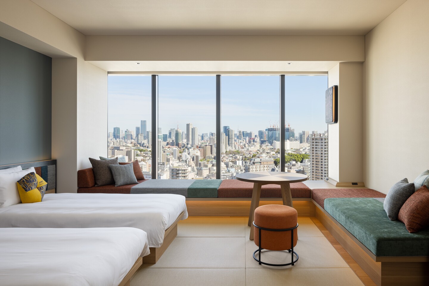 Guest room with two beds and window seat beside large windows with view of Tokyo skyline