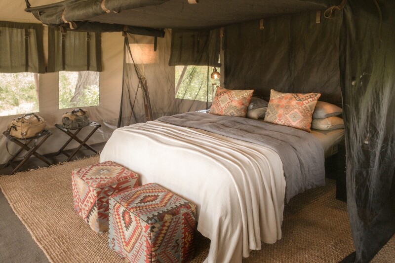 Guest bedroom at Nyasi Tented Camp, with canvas walls and windows and colorful, patterned pillows and furnishings