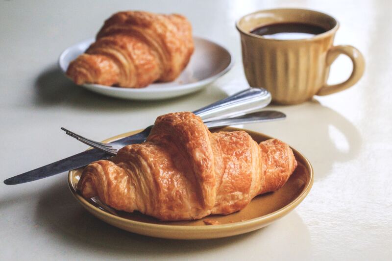Two French croissants on plates with a cup of black coffee in the background.