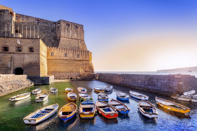 Colorful boats floating outside of a historic castle in Naples, Italy