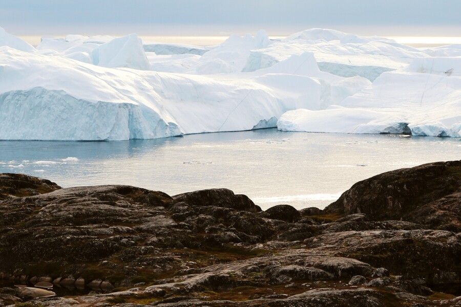View from bare ground of water, with glaciers in background in 
Greenland