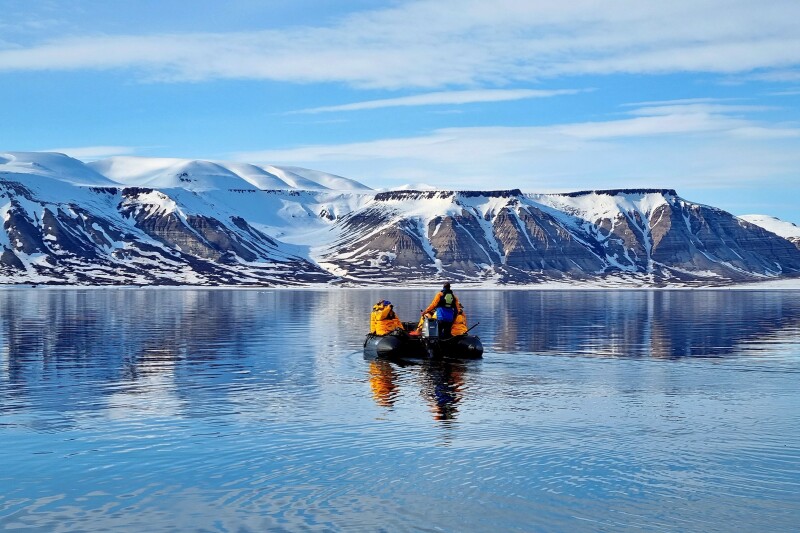People in a Zodiac floating on the water in Svalbard with snowy mountains in the distance