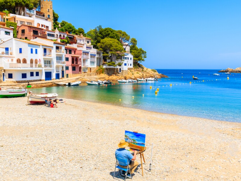 A painter working at an easel on otherwise empty Sa Tuna beach near Barcelona in Begur