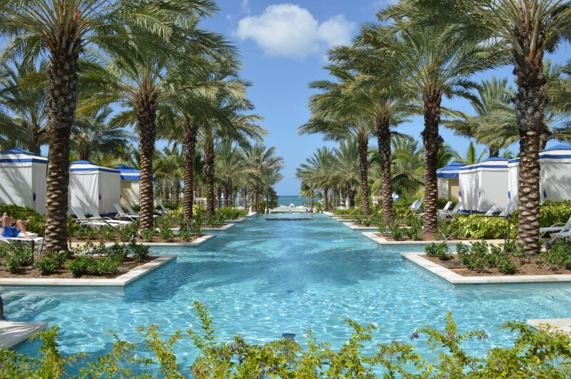 Large pool area at Baha Mar, Bahamas with a row of blue and white cabanas and palm trees on each side