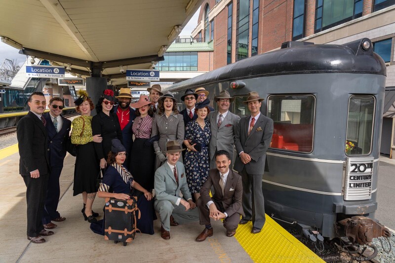 Passengers dressed in 1940s-style clothes beside train.