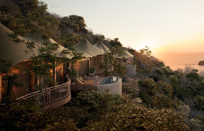 Luxury tents with private balconies to the left look out over a sloping hill and the ocean at Nekajui Camp