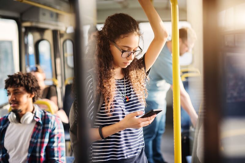 A woman riding on a bus texts on her phone.