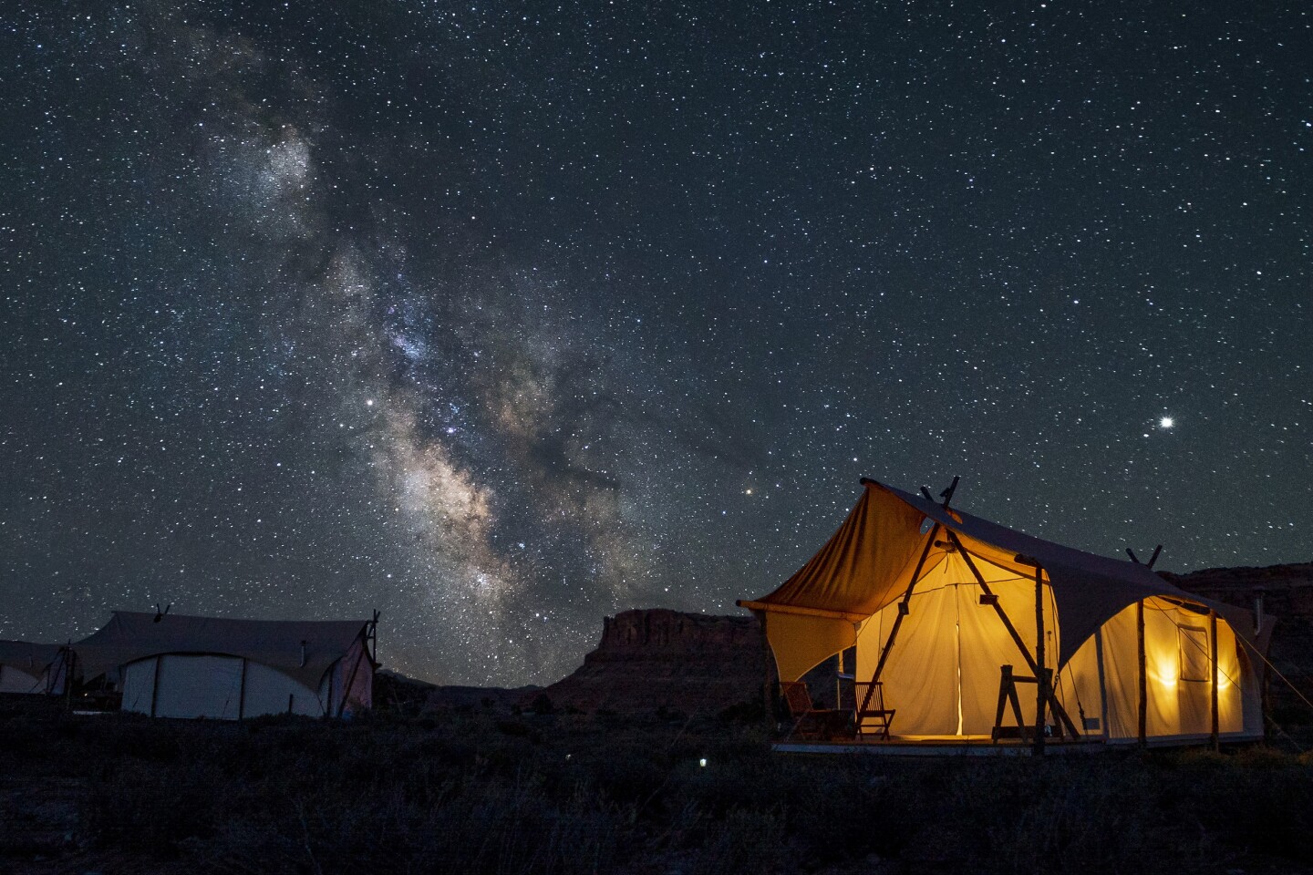 A tent accommodation at Under Canvas Moab with lighting inside the tent and a clear view of stars in the night sky above