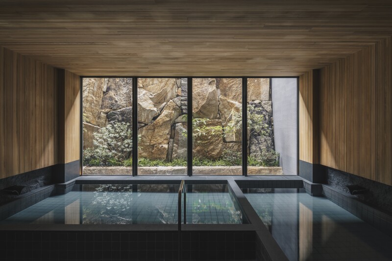 Wood-paneled bathhouse area of the spa at Six Senses Kyoto, with floor-to-ceiling windows overlooking rock-walled garden