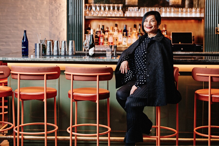 Dressed in black, Chutatip “Nok” Suntaranon, chef and restaurateur at Kalaya, is seated on a bar stool.