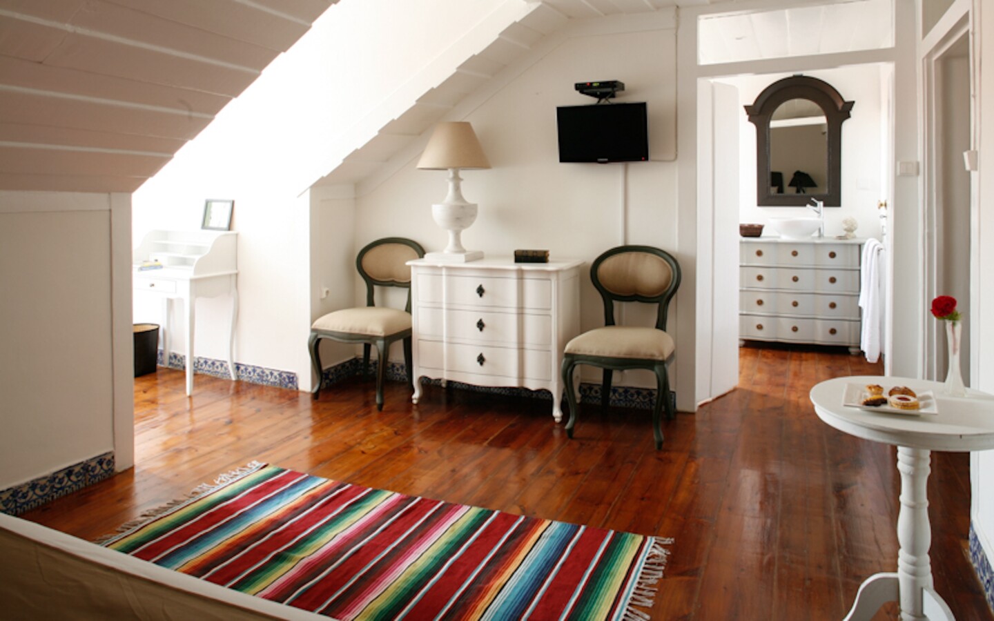 Guest room interior at Palácio Ramalhete, with wooden floor, white dresser, and colorful, striped carpet