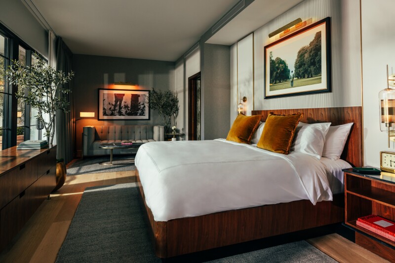 Bed facing floor-to-ceiling windows in a hotel room with a green-and-brown palette