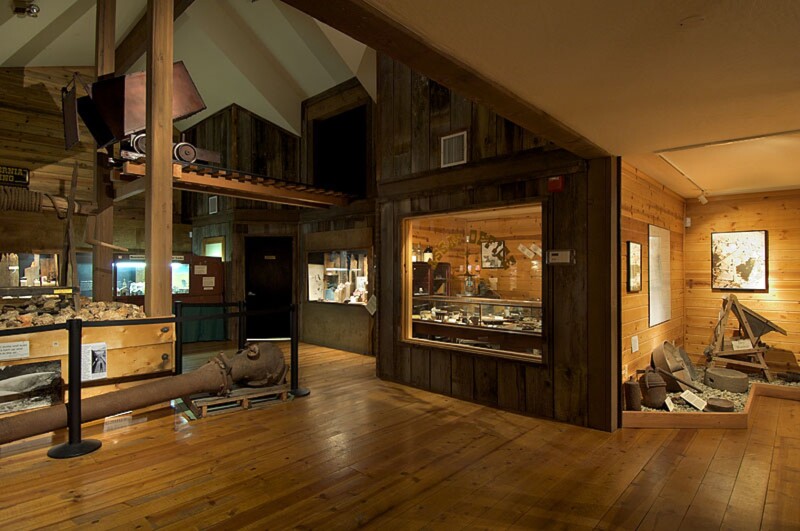 Mining artifacts are displayed in a section of the California State Mining and Mineral Museum. Wood floors and wood panels line the walls.