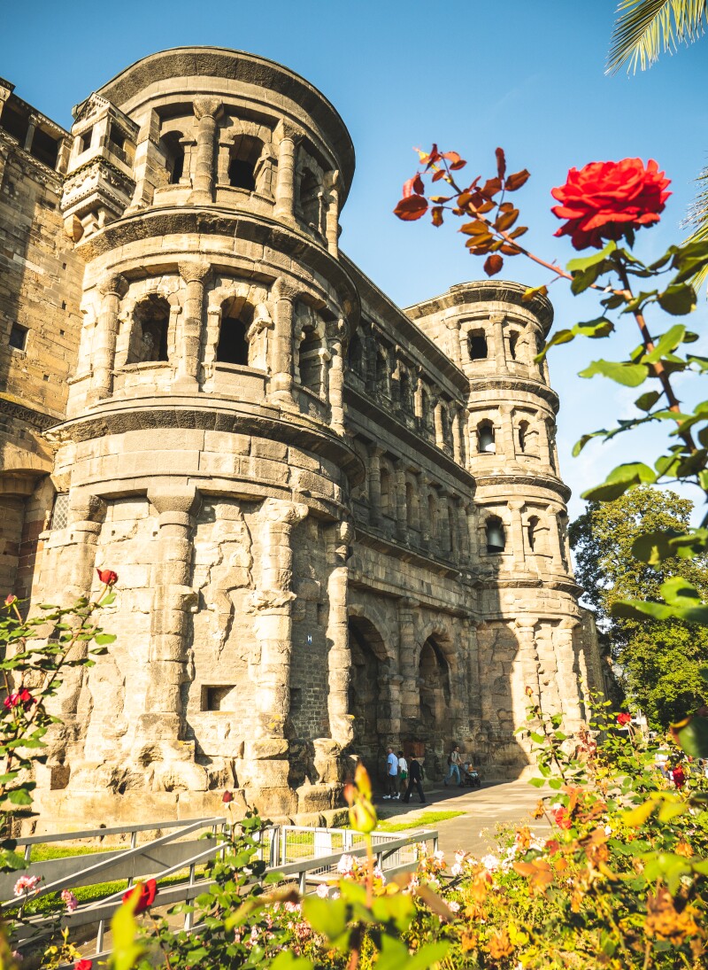 A photograph of Porta Nigra in Trier in Germany with a red rose in the foreground.