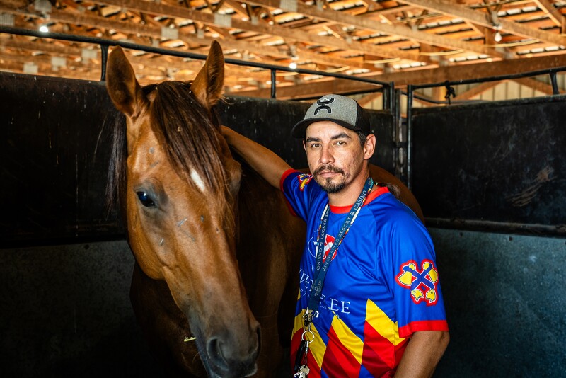 Portrait of brown horse and man with goatee wearing a hat and blue, yellow, and red jersey