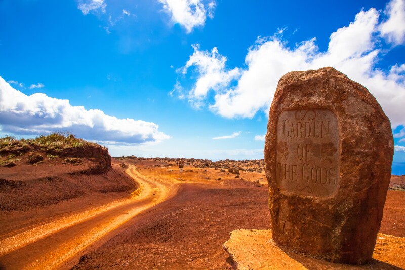 Red boulder inscribed "Garden of the Gods", beside red dirt road