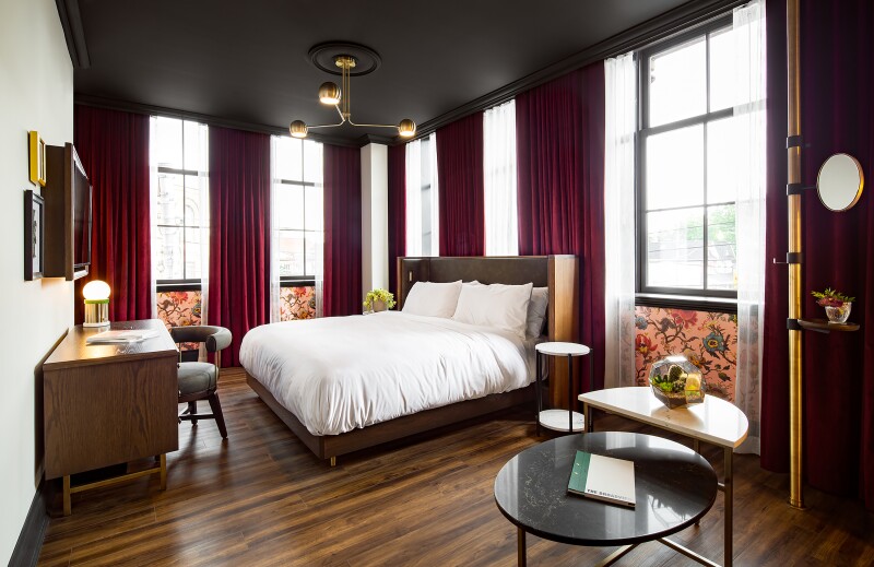 A King Corner Room, with dark wood floor and floral wallpaper below several windows with red velvet curtains