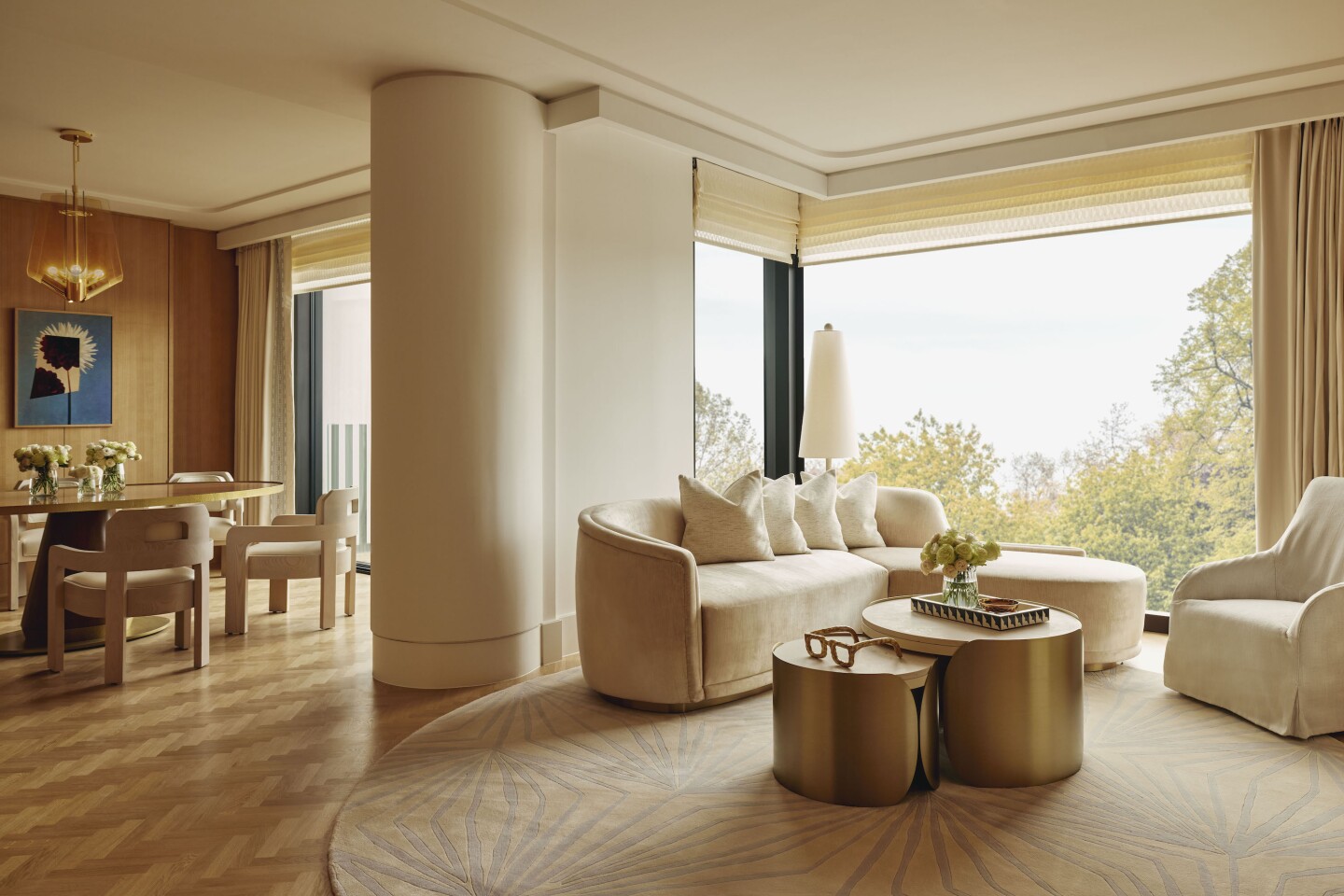 A living area of a suite, with white circular rug and a white couch facing floor-to-ceiling windows