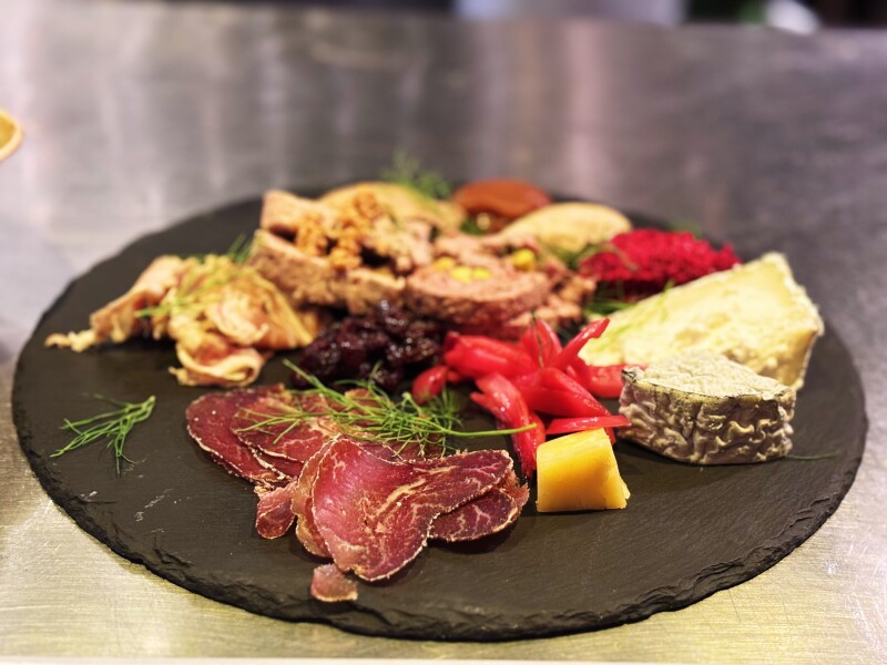 A dark plate of charcuterie and cheese with herbs and peppers