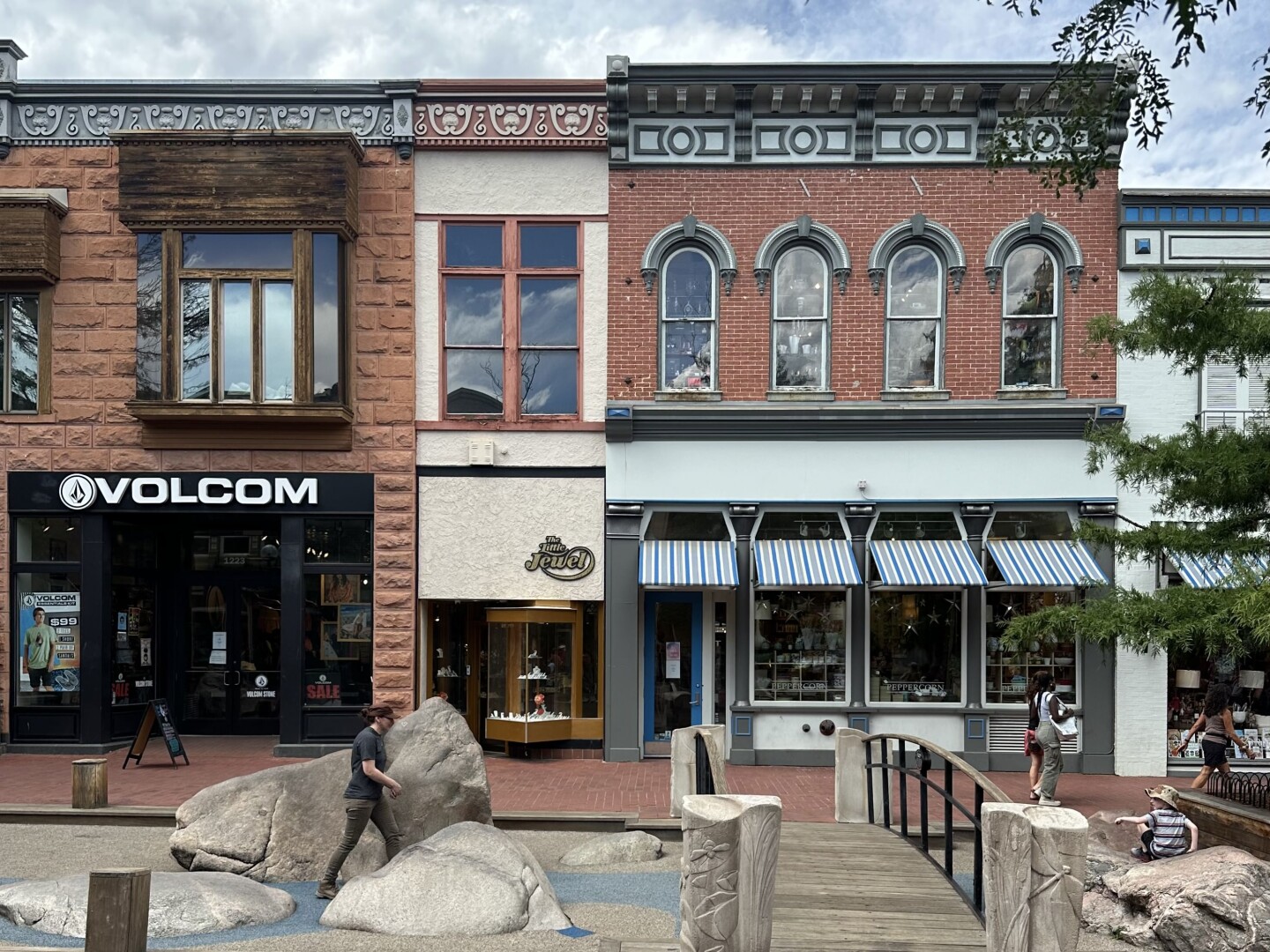 A pedestrian mall of two-story historic buildings, with boulders and footbridge in foreground