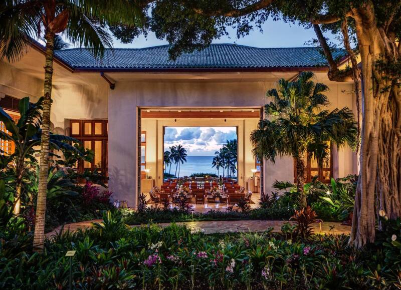 Distant view of ocean through courtyard of greenery at Grand Hyatt Kauai at twilight