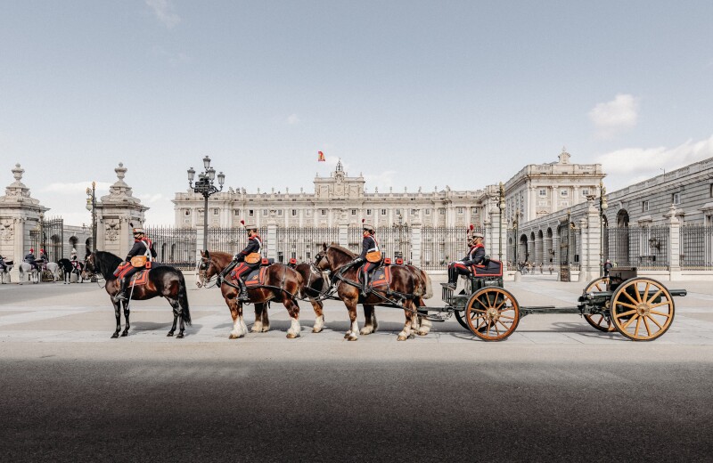 Riders in formal guardsman clothing on horses drawing a carriage in front of the Royal Palace, Madrid, Spain.