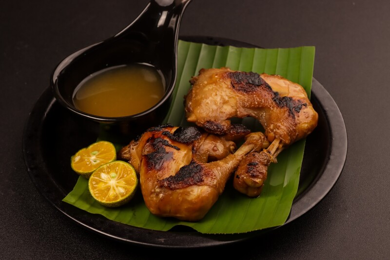 Grilled chicken on a plate with calamansi and brown sauce in a deep black spoon