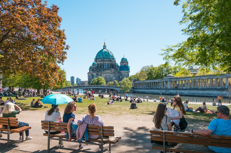 People on benches in foreground in public park, with Museum Island and Berlin Cathedral in distance