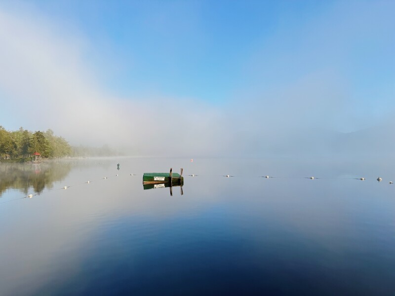 Small floating green dock in flat, misty lake