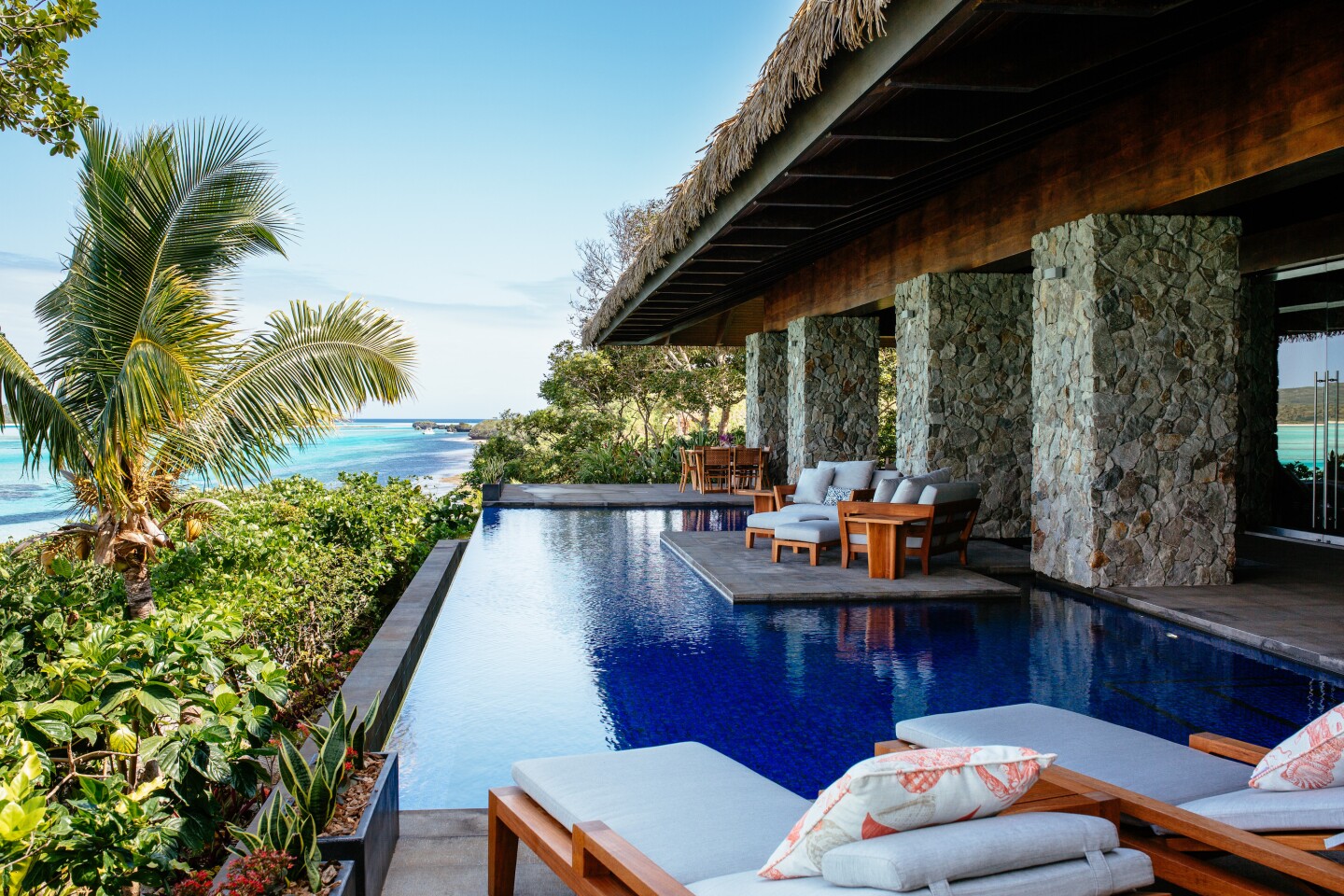 The Delana Villa’s infinity pool at Vatuvara Private Islands Resort, with several empty white lounge chairs on deck, with ocean in distance
