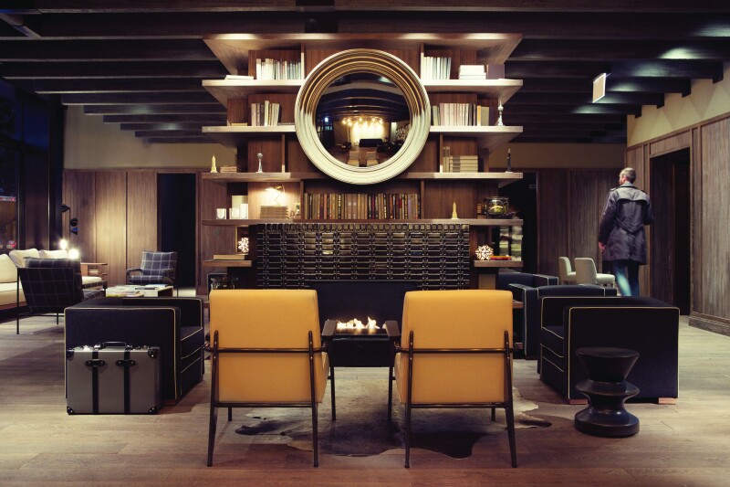 The lobby of the Thompson Chicago, with black and mustard-colored chairs centered on a gas fireplace, with bookshelves above it