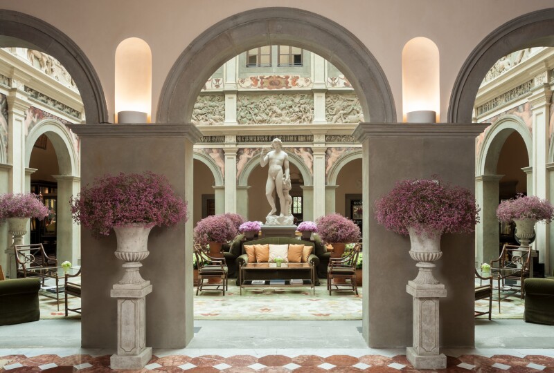 The entrance of the Four Seasons Hotel Firenze features a statue of Bacchus and large floral arrangements.