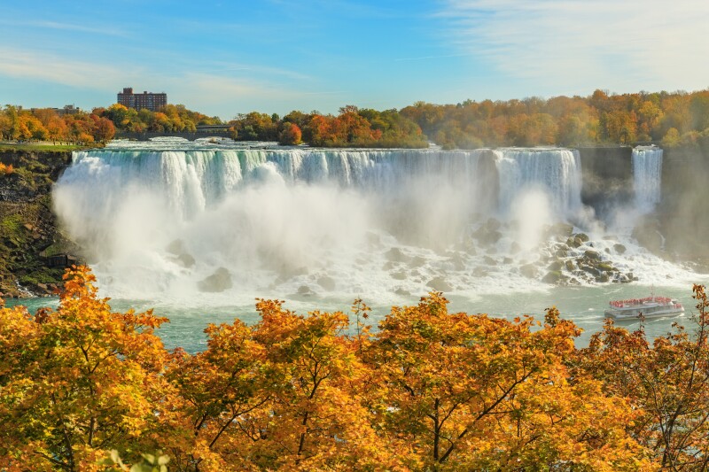 Niagara Falls with orange fall trees in the foreground and surrounding the falls and a tour boat at base of falls