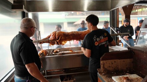 Two men behind a roasted pork on a spit