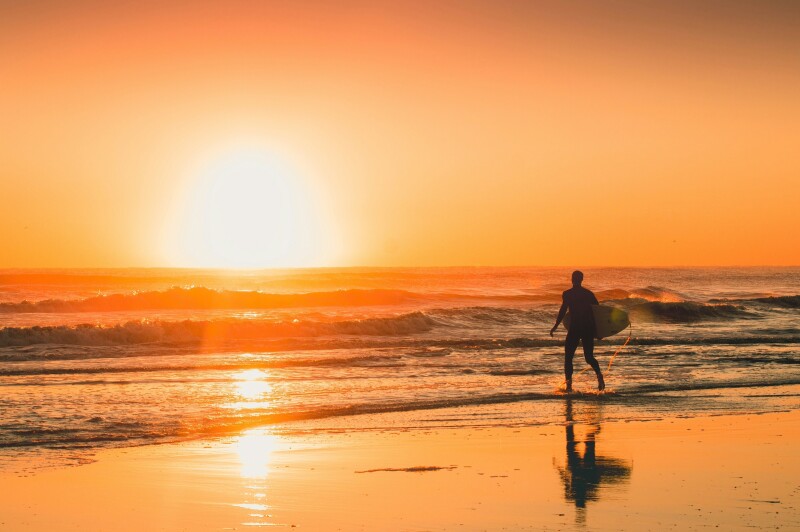 A surfer jogging into the water at sunset on Jacksonville Beach, Florida