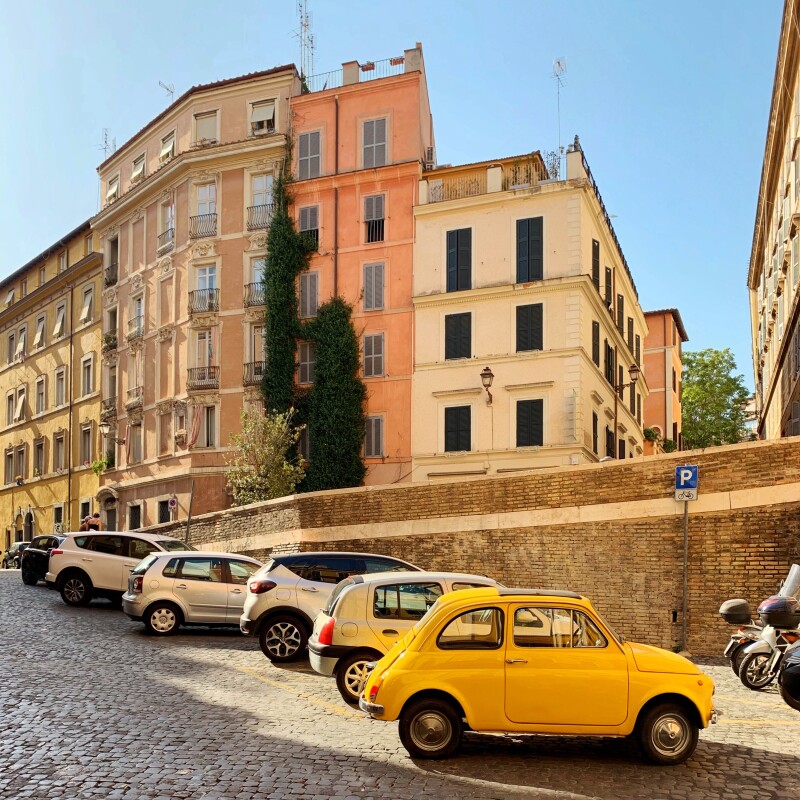 A yellow Fiat 500 at front of row of parked cars in a residential neighborhood