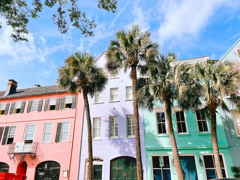 A row of pink, purple, and turquoise historic buildings in Charleston with palm trees in front of them