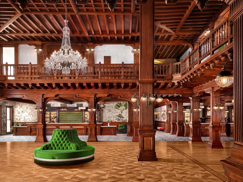 The restored two-story wood lobby with circular green chaise lounge under a chandelier