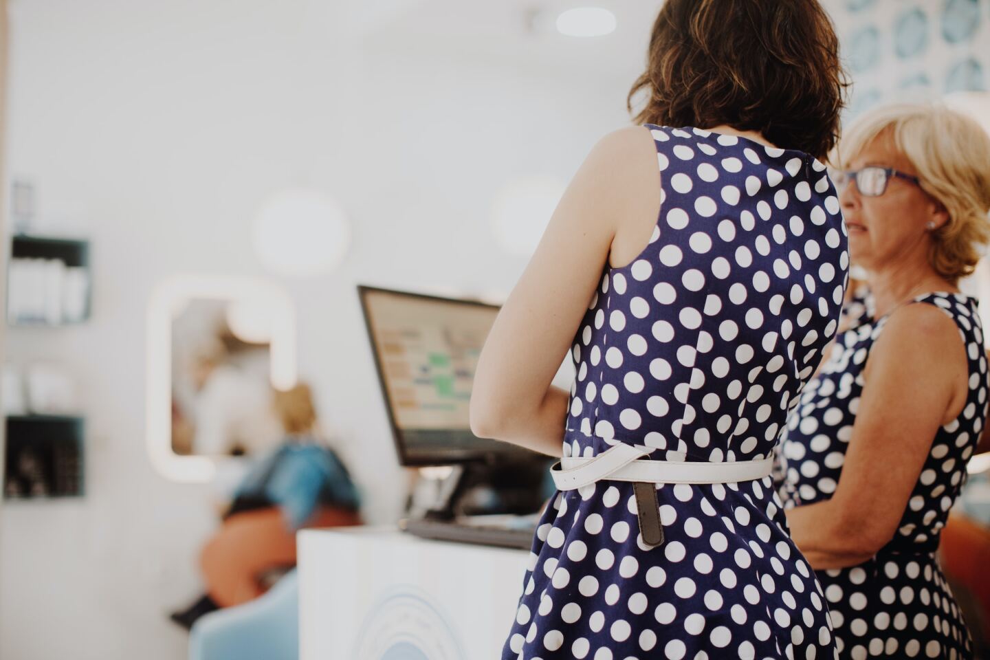 Two women in navy and white polka dot dresses chatting near a computer