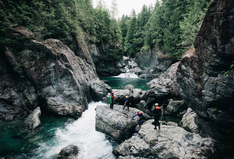 A family wearing helmets standing on boulders beside narrow river and forest