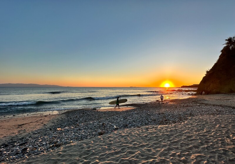 Man carrying surfboard on beach at sunset