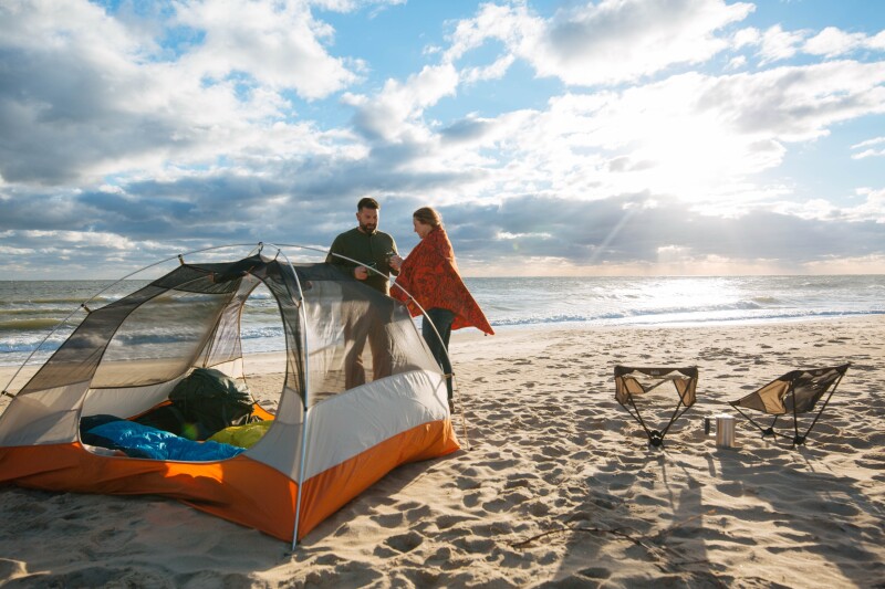 A couple standing outside of a tent on the beach at camping at False Cape State Park in Virginia Beach, Virginia.
