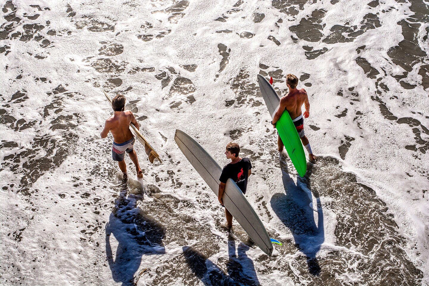 Overhead view of three California surfers headed into the water with their boards