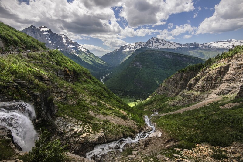 A green river valley in Glacier National Park, with small stretch of Going-to-the-Sun-Road at left on steep hillside